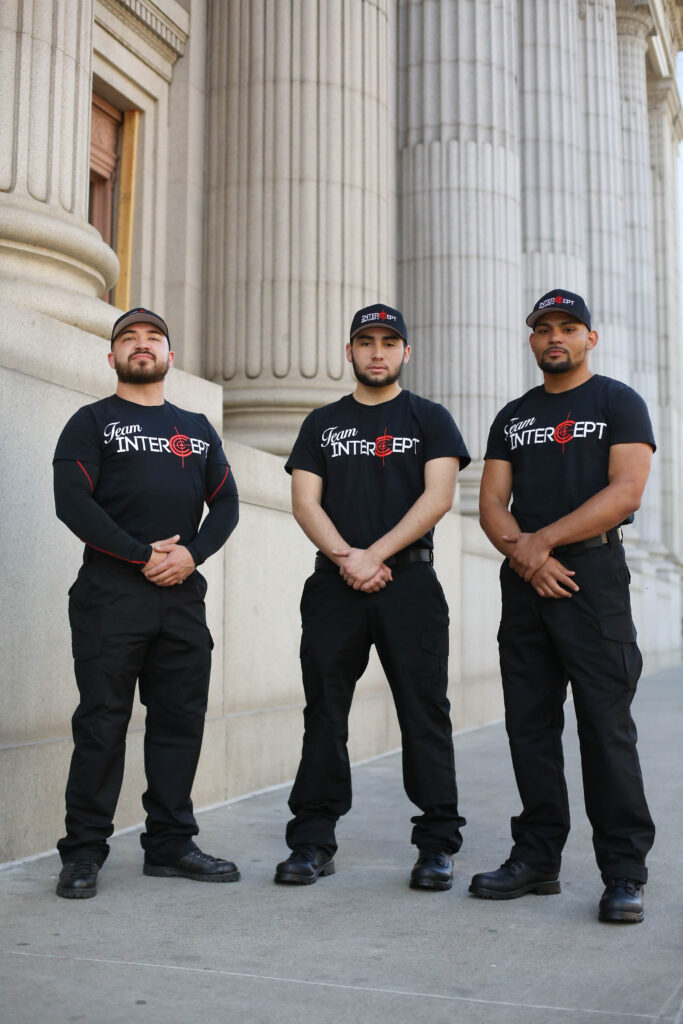 3 men wearing "Team Intercept" black T-shirts and black pants in front of a building