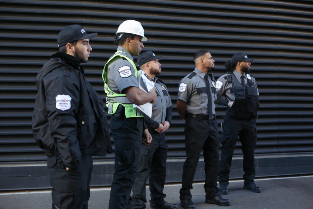 Five Intercept Security guards in full uniforms standing in front of an external metal wall while looking to the right